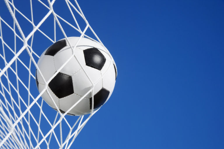 Soccer ball in the goal net against blue sky background